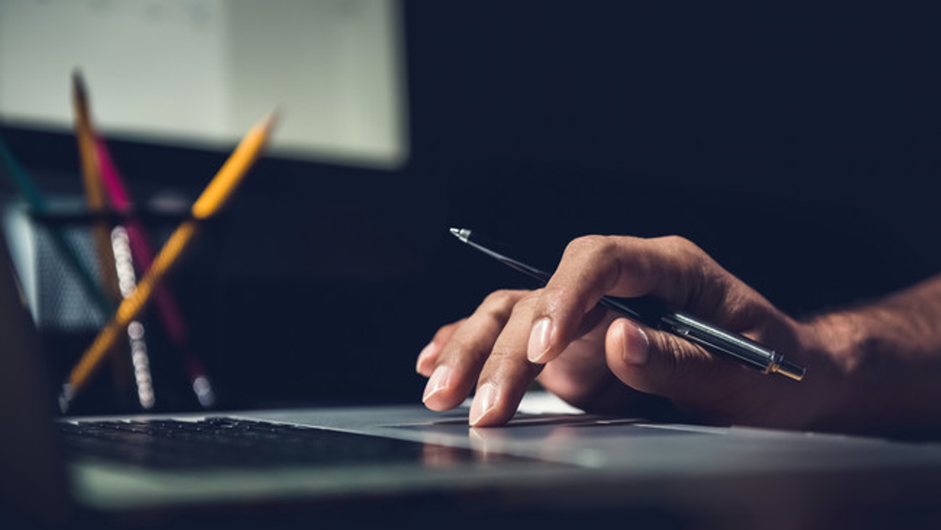 image: hand holding a pen in front of keyboard