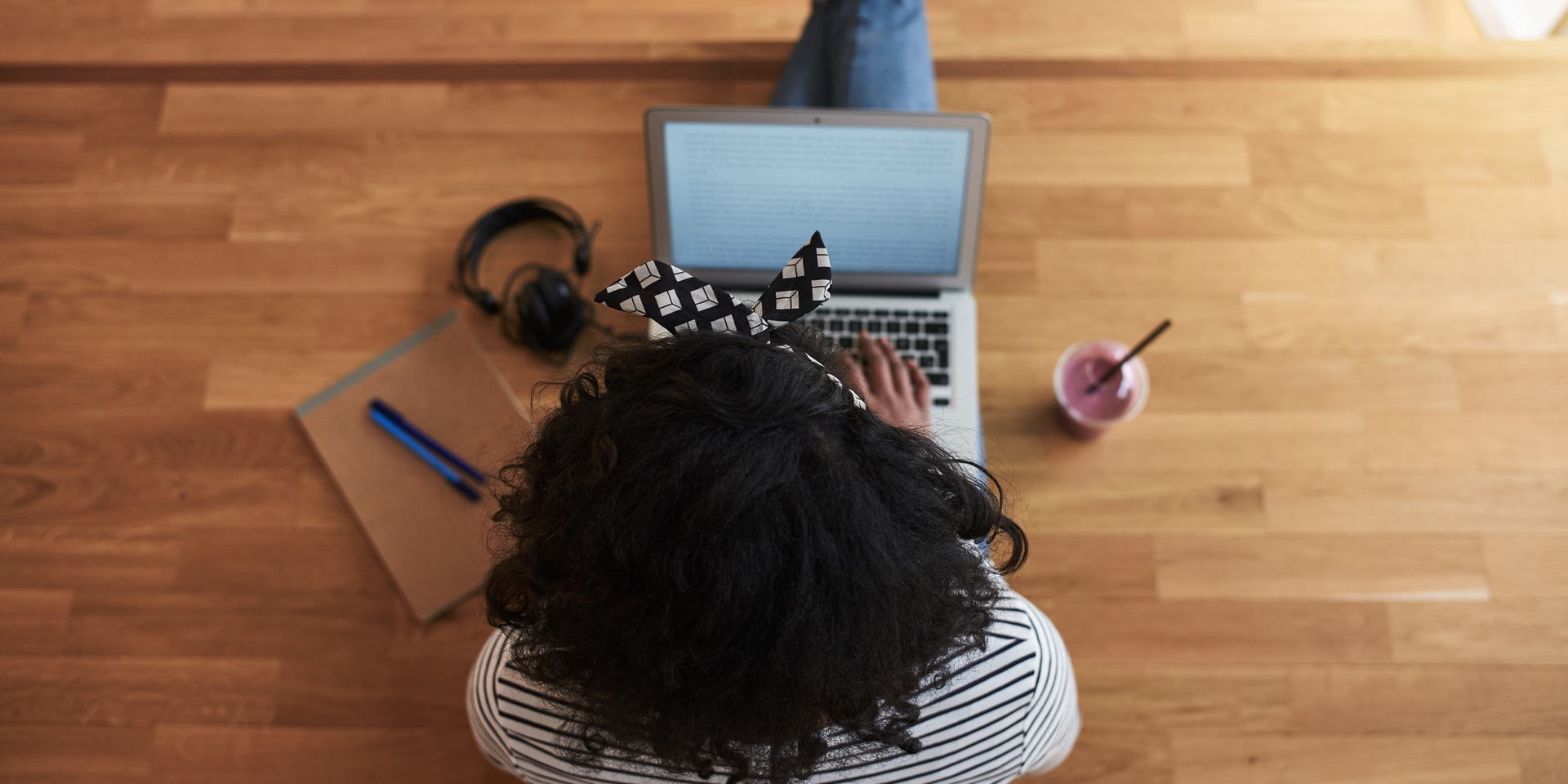 Person using laptop with notebook, earphones and drink